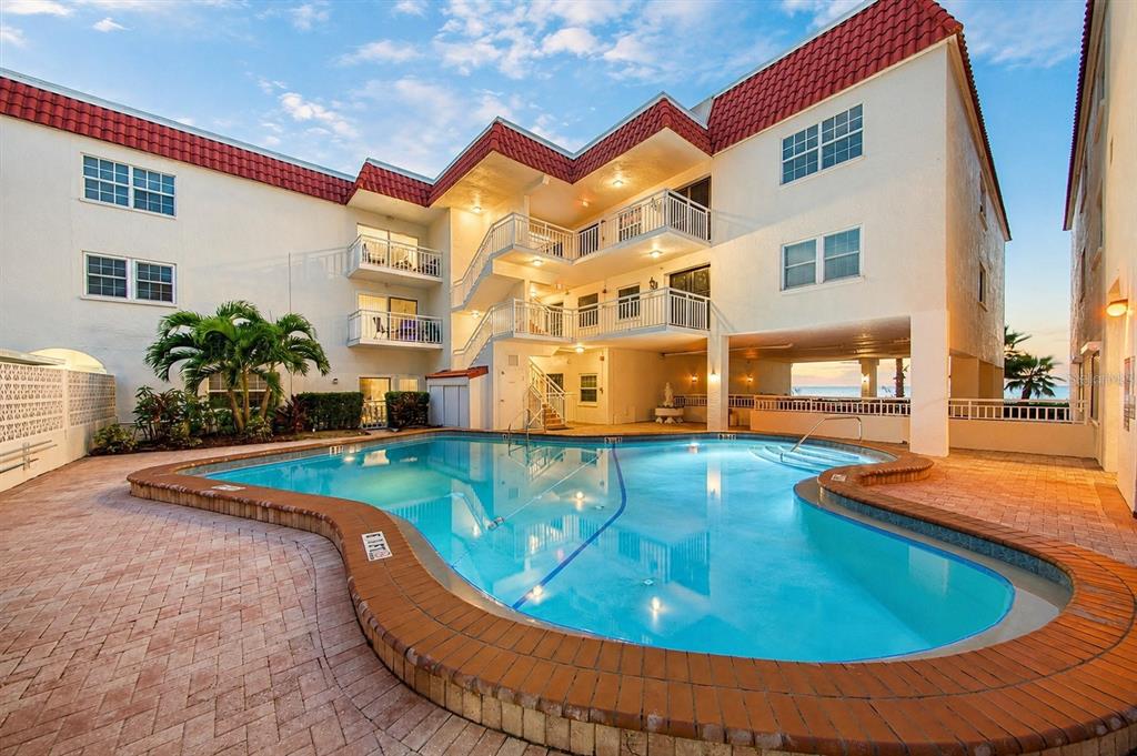 A multi-story apartment building with a red tile roof overlooks a curved swimming pool — 2900 GULF BOULEVARD UNIT 108, BELLEAIR BEACH, FL