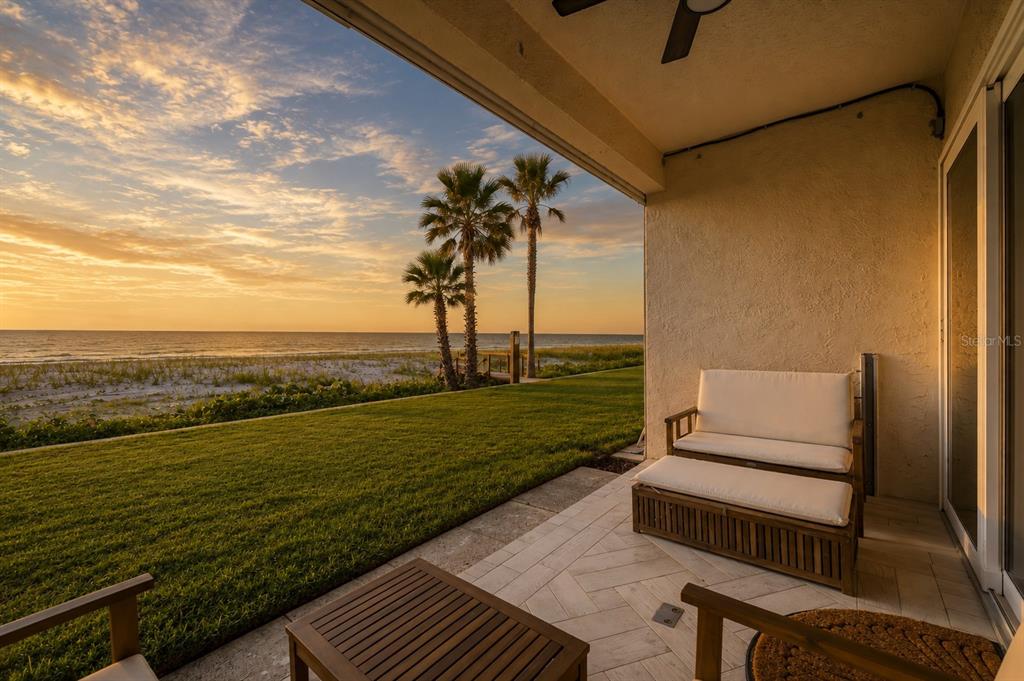 A patio with a wooden bench and table overlooks a grassy lawn and the ocean — 2900 GULF BOULEVARD UNIT 108, BELLEAIR BEACH, FL