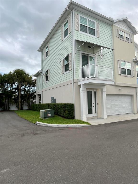 A three-story townhouse with light green siding, a small balcony, and an attached garage — 821 OAK BEND LANE, DUNEDIN, FL