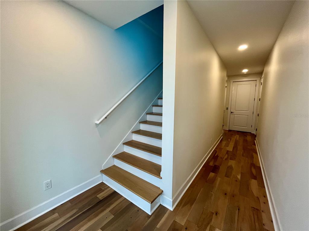 A hallway features hardwood floors, a white door, and a staircase with wooden treads — 821 OAK BEND LANE, DUNEDIN, FL