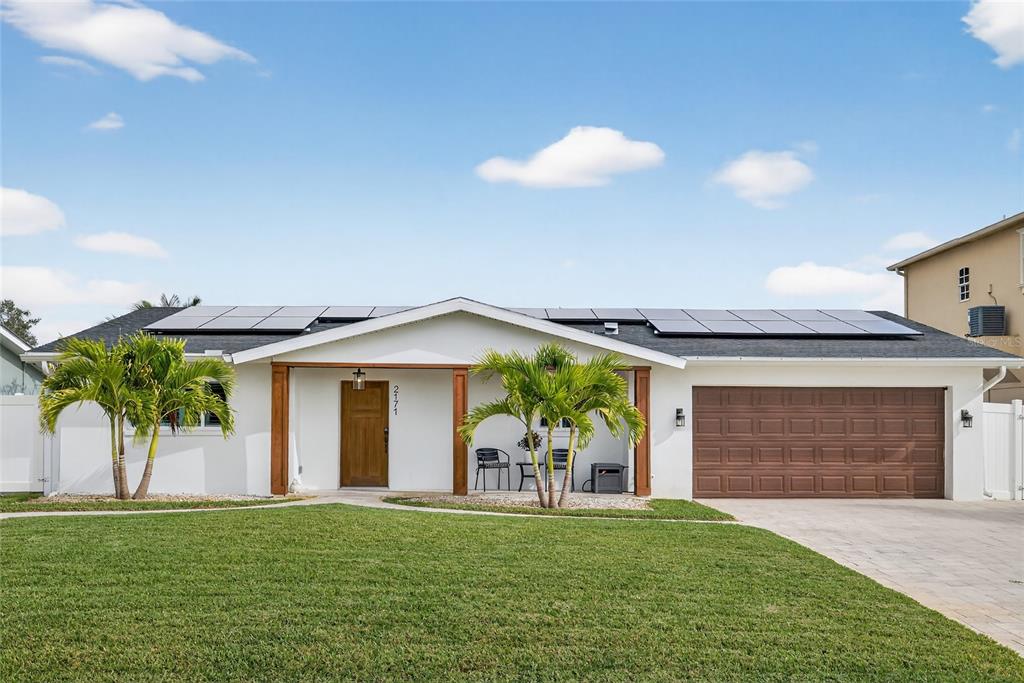 A single-story white house with a brown garage door, wooden porch posts, and roof solar panels — 2171 LAGOON DRIVE, DUNEDIN, FL