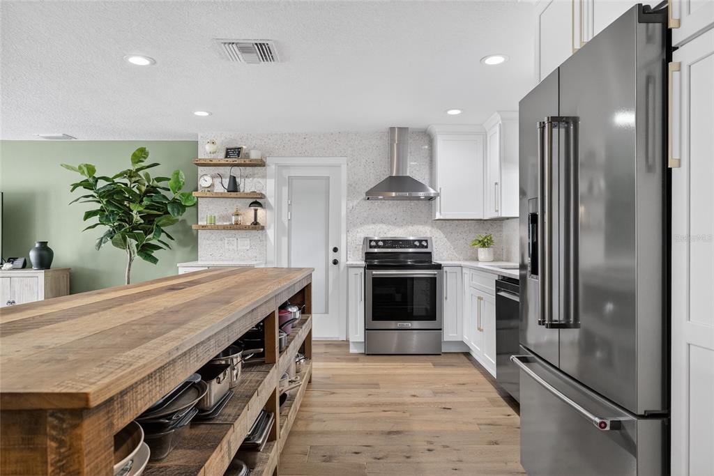 A modern kitchen features a wooden island, stainless steel appliances, and white cabinetry — 2171 LAGOON DRIVE, DUNEDIN, FL