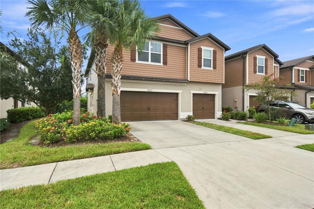 A two-story townhouse with brown siding, a two-car garage, and palm trees in the front yard — 9237 HILLCROFT DRIVE, RIVERVIEW, FL