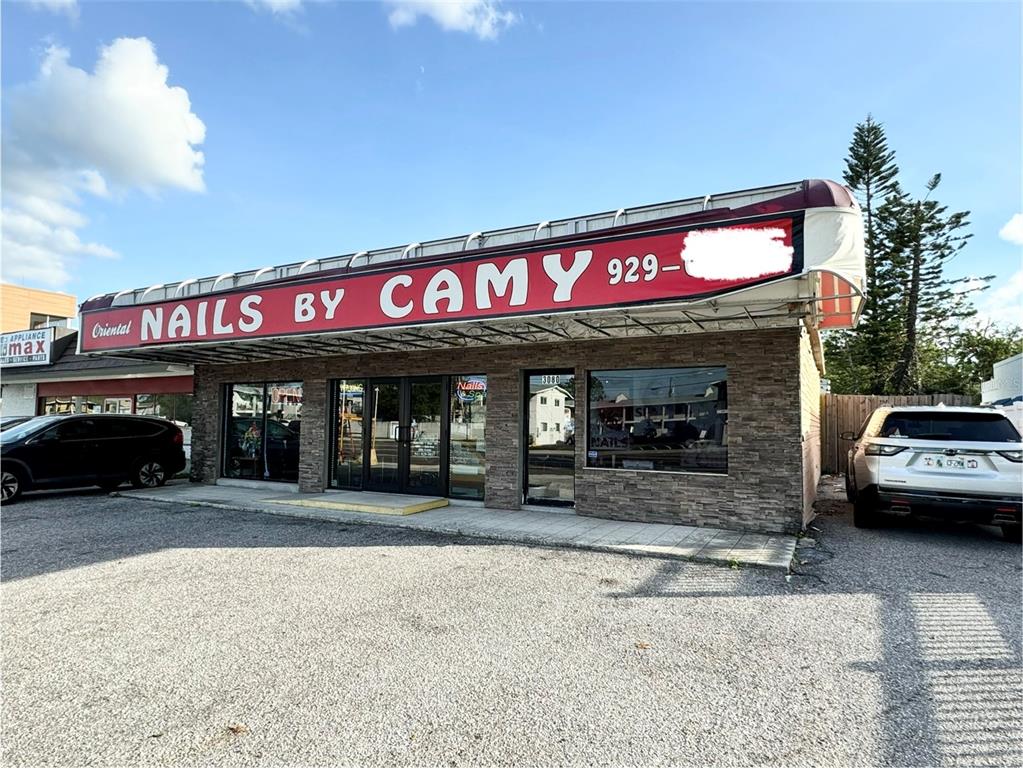 The exterior of a commercial building features a red sign reading Nails by Camy — 3080 BEE RIDGE ROAD, SARASOTA, FL