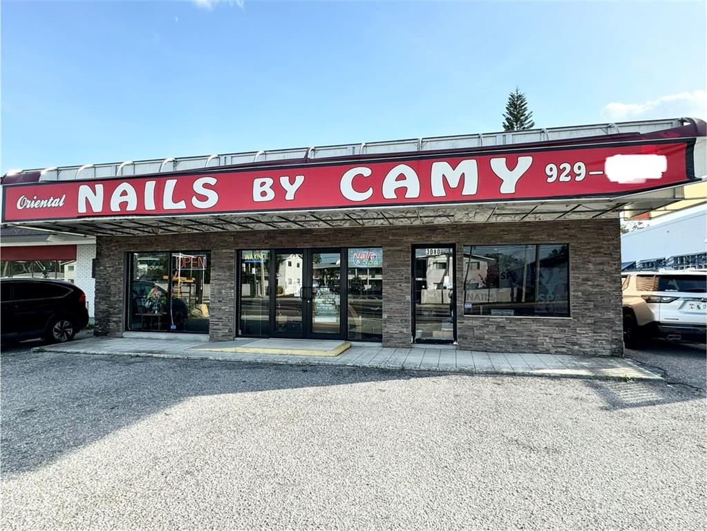 The exterior of a commercial building features a red sign reading Nails by Camy — 3080 BEE RIDGE ROAD, SARASOTA, FL
