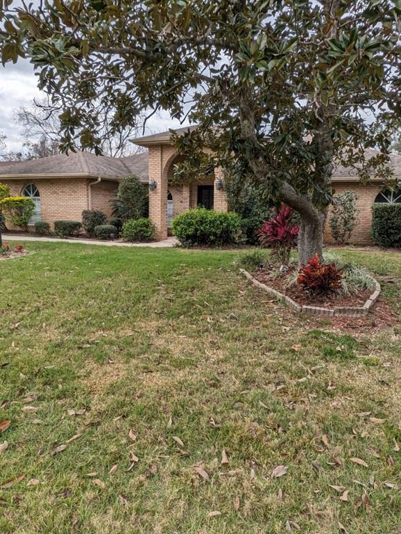 A single-story brick house features an arched entryway and a large tree in the front yard — 72 SPRING LAKE DRIVE, DEBARY, FL