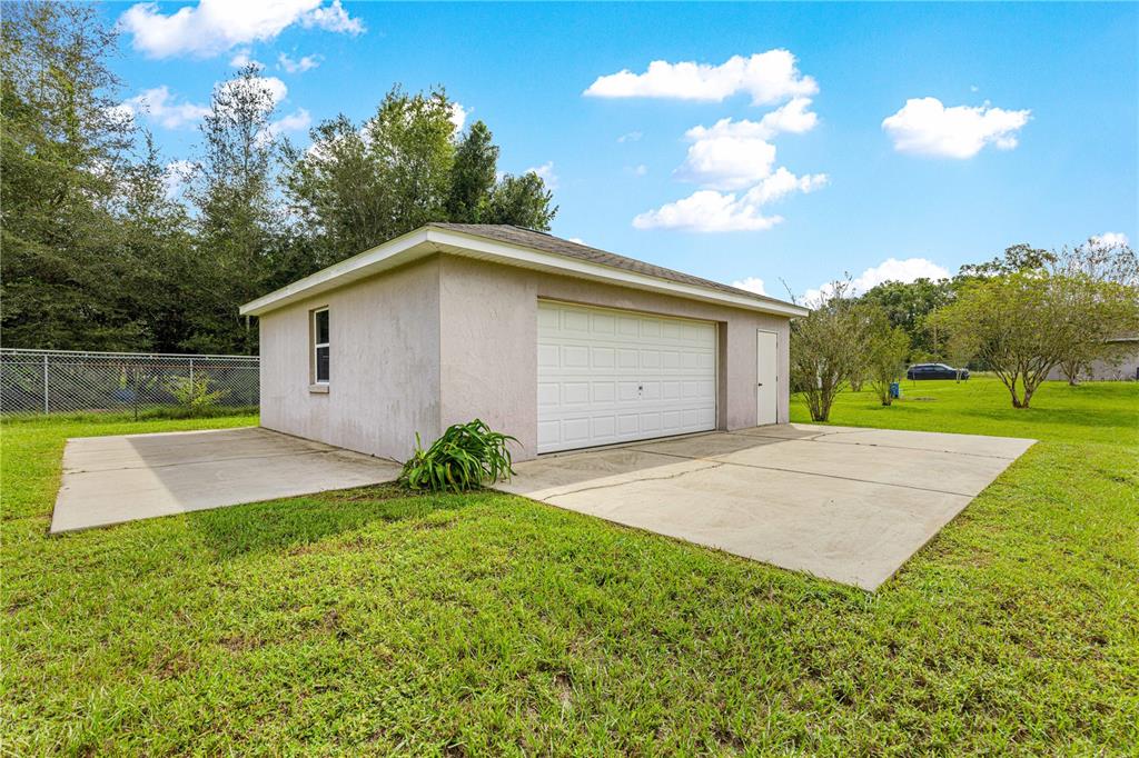 A detached garage with a white door, side entrance, and concrete driveway on a grassy lot — 3805 SE 139TH STREET, SUMMERFIELD, FL