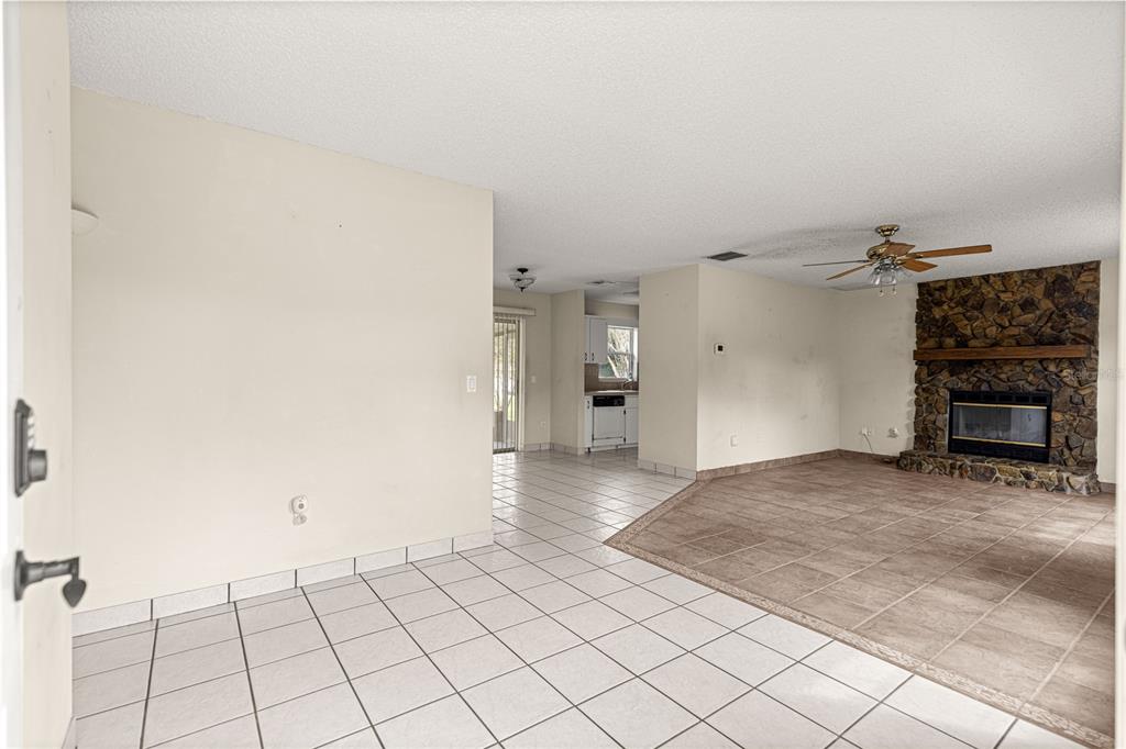 An open-concept living area features light tile flooring, a stone fireplace, and a kitchen beyond — 3805 SE 139TH STREET, SUMMERFIELD, FL