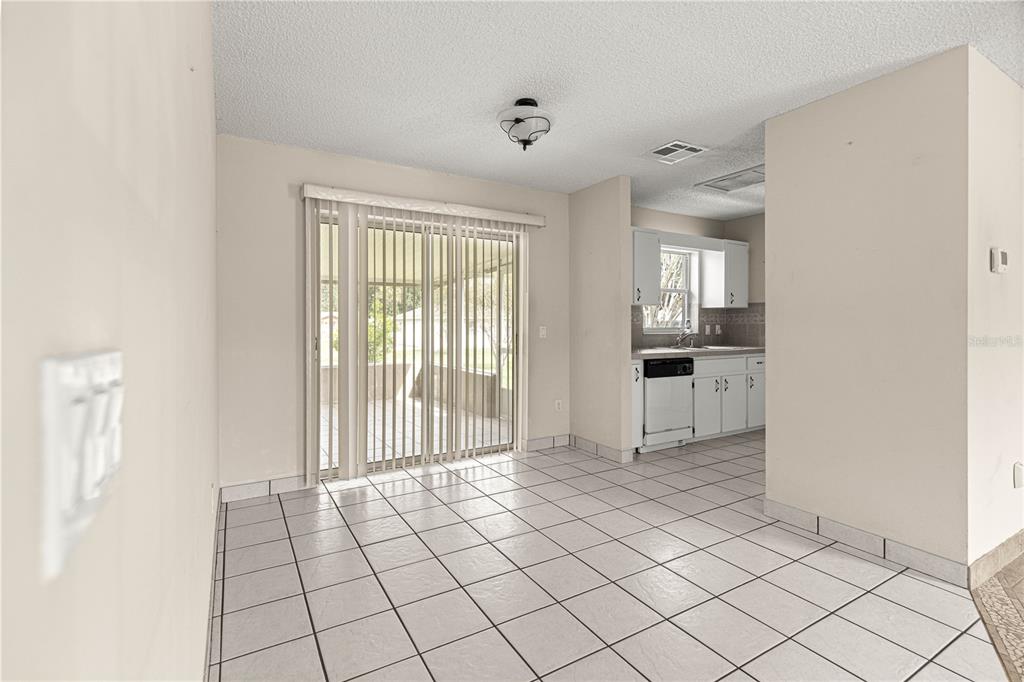 A dining area with white tile floors, a sliding glass door, and an adjacent kitchen — 3805 SE 139TH STREET, SUMMERFIELD, FL
