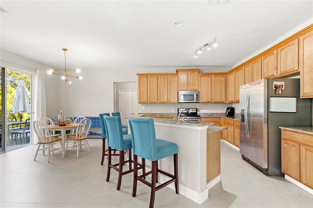 A kitchen with light wood cabinets, granite countertops, and a breakfast bar with blue stools — 5045 BALLARK STREET, MOUNT DORA, FL