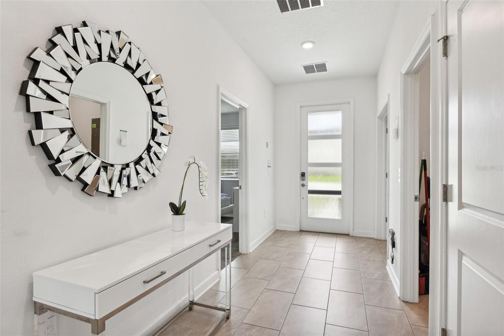 A bright entryway features a white console table, a decorative sunburst mirror, and tiled flooring — 9266 SOMMERSET HILLS DRIVE, DAVENPORT, FL