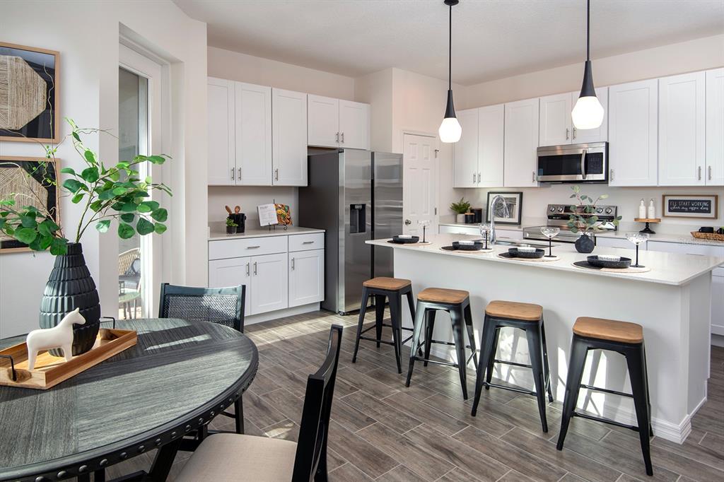 A modern kitchen features white cabinetry, stainless steel appliances, a center island, and wood-look flooring — 1532 SILVER LINING WAY, APOPKA, FL