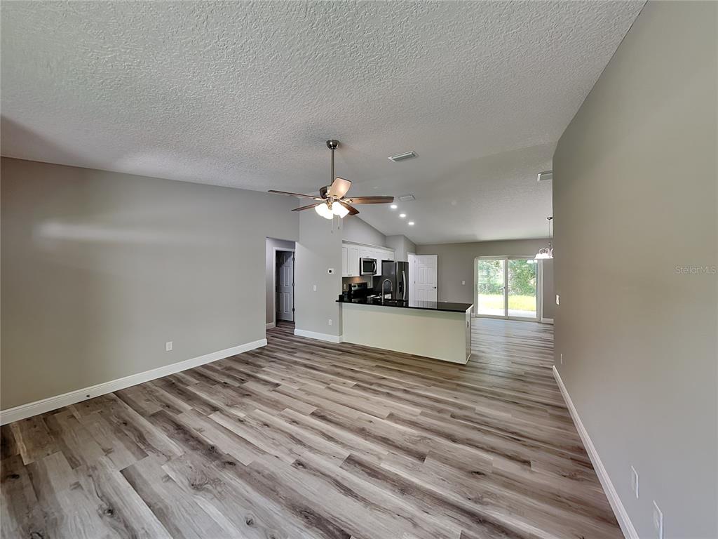 An open-concept living area features wood-look flooring, a ceiling fan, and a kitchen with a peninsula — 9399 N DEL RIO WAY, DUNNELLON, FL
