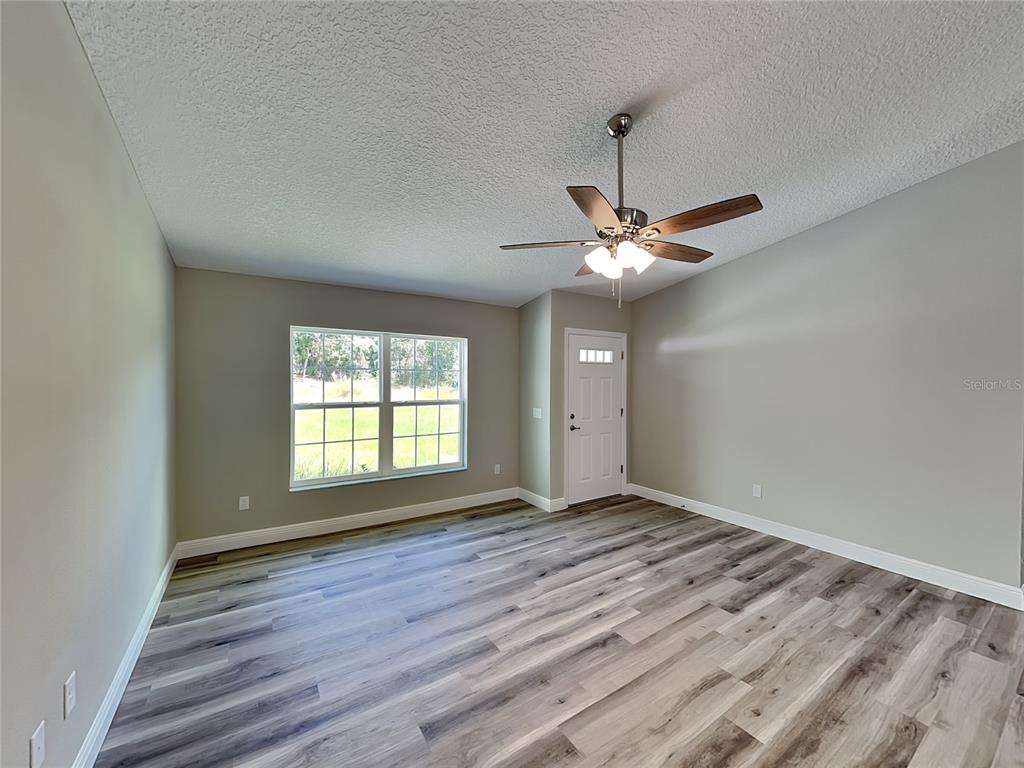 An empty room features light gray walls, wood-look flooring, a ceiling fan, and a door — 9399 N DEL RIO WAY, DUNNELLON, FL