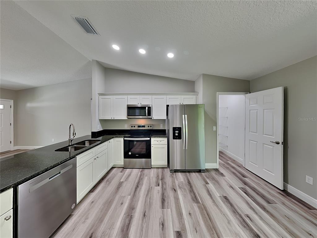 A kitchen features white cabinets, stainless steel appliances, dark countertops, and light wood-look flooring — 9399 N DEL RIO WAY, DUNNELLON, FL