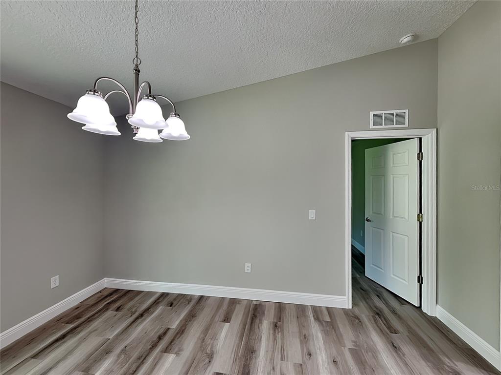 An empty room with gray walls, wood-look flooring, and a hanging chandelier — 9399 N DEL RIO WAY, DUNNELLON, FL