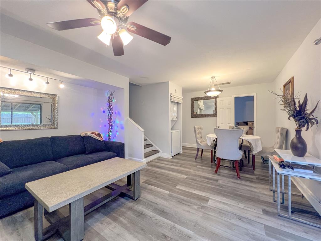 A living and dining area features gray wood-look flooring, a dark sofa, and a staircase — 12414 N 58TH STREET UNIT 63, TAMPA, FL