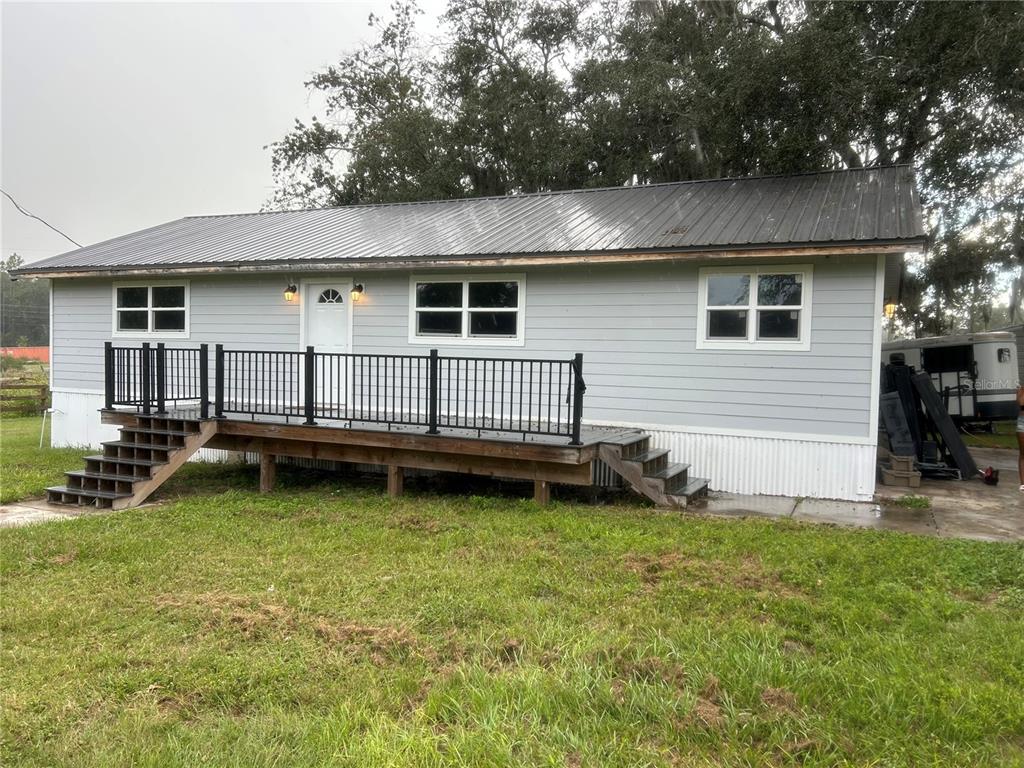 A light gray single-story house with a metal roof and a wooden deck with railings — 10661 W HIGHWAY 40, OCALA, FL