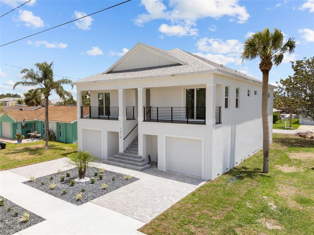 A white two-story house with a raised porch, black railings, and a paved driveway — 7414 MAKO DRIVE, HUDSON, FL
