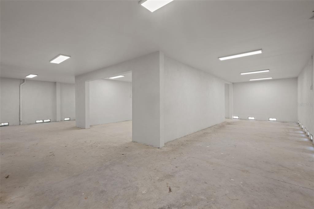 An empty, unfinished basement room features white walls, concrete floors, and multiple ceiling light fixtures — 7414 MAKO DRIVE, HUDSON, FL