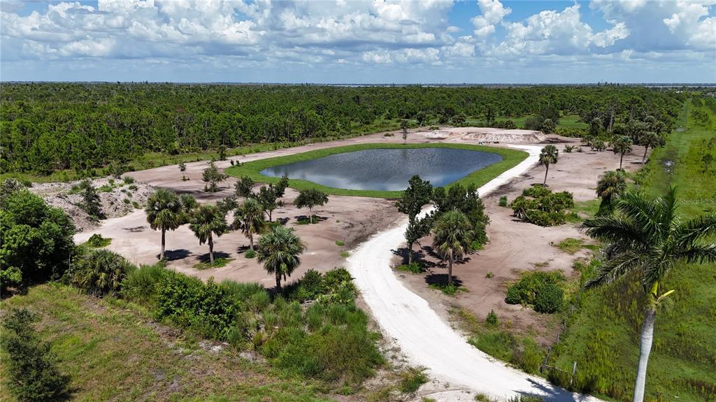 An aerial view shows a dirt road leading to a pond surrounded by cleared land — 6455 STRINGFELLOW ROAD, ST JAMES CITY, FL