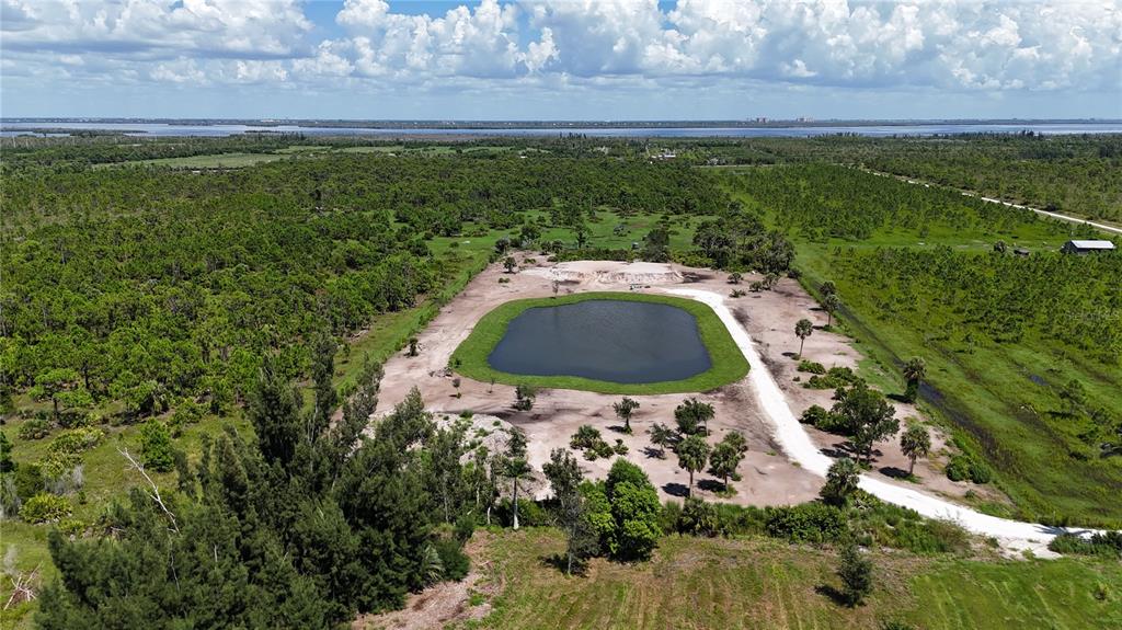An aerial view shows a pond surrounded by cleared land and dense vegetation — 6455 STRINGFELLOW ROAD, ST JAMES CITY, FL
