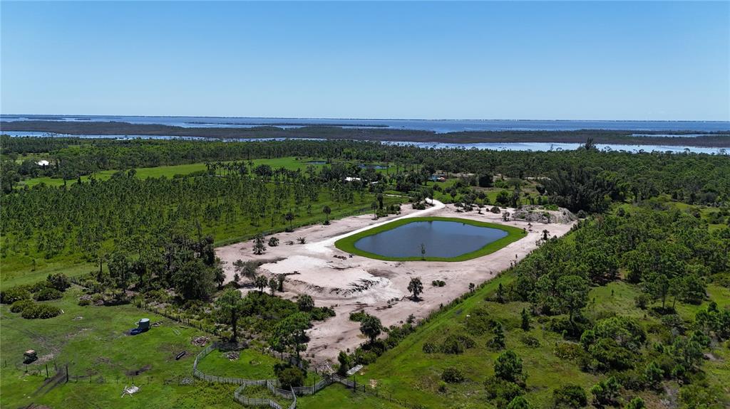 An aerial view shows a pond surrounded by cleared land, trees, and a distant waterway — 6455 STRINGFELLOW ROAD, ST JAMES CITY, FL