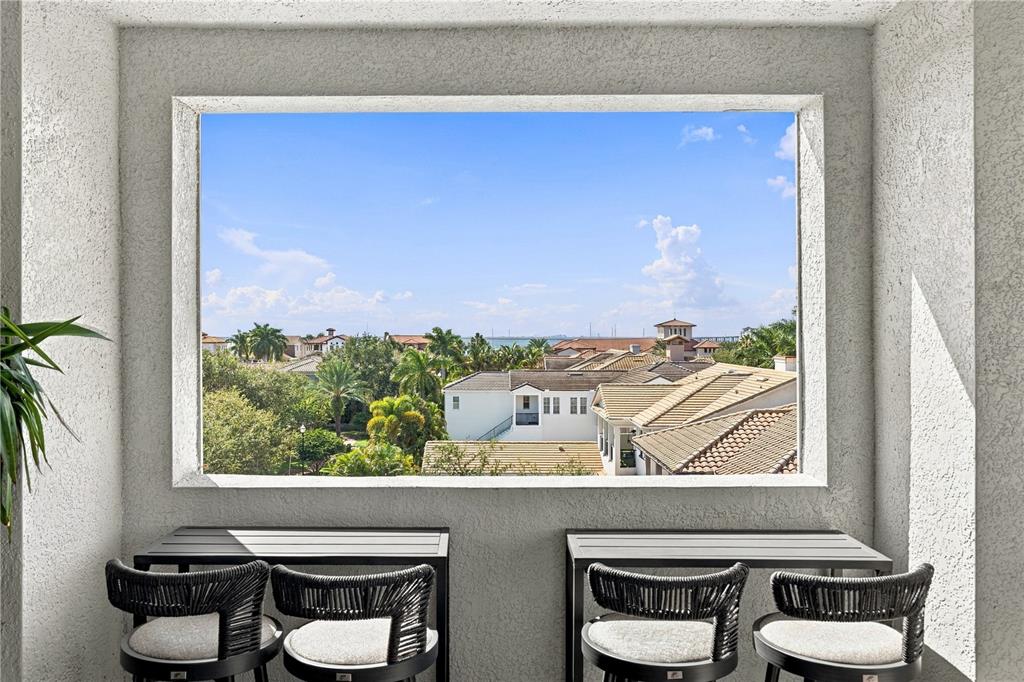 A balcony with two small tables and four chairs overlooks a neighborhood and distant water — 6002 YEATS MANOR DRIVE UNIT 101, TAMPA, FL