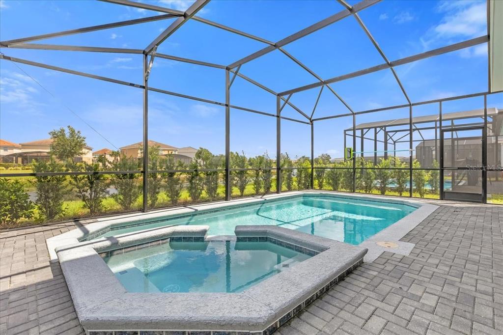 A screened-in patio features a swimming pool and an attached hot tub on pavers — 7211 OAKMOSS LOOP, DAVENPORT, FL