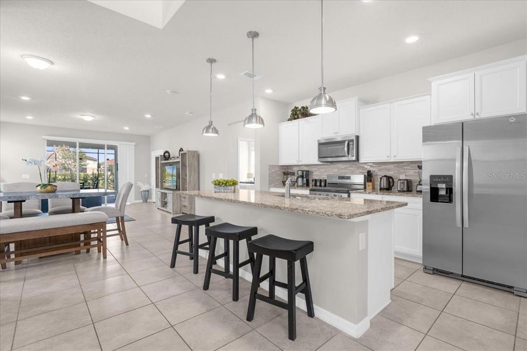 A kitchen with white cabinets, granite countertops, and a breakfast bar with three black stools — 7211 OAKMOSS LOOP, DAVENPORT, FL