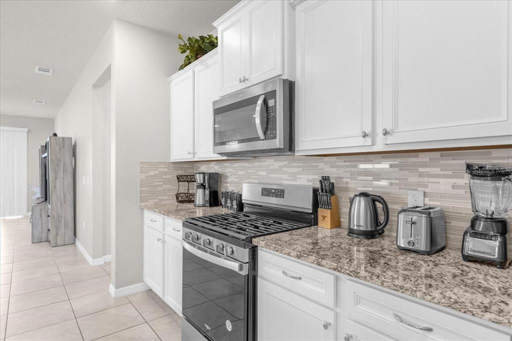 A kitchen features white cabinets, granite countertops, a stainless steel stove, and a tiled backsplash — 7211 OAKMOSS LOOP, DAVENPORT, FL