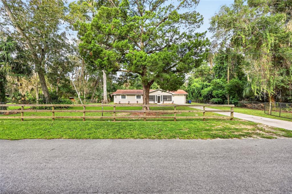 A single-story house sits behind a wooden fence and a large tree in the yard — 1920 NW 15TH AVENUE, CRYSTAL RIVER, FL