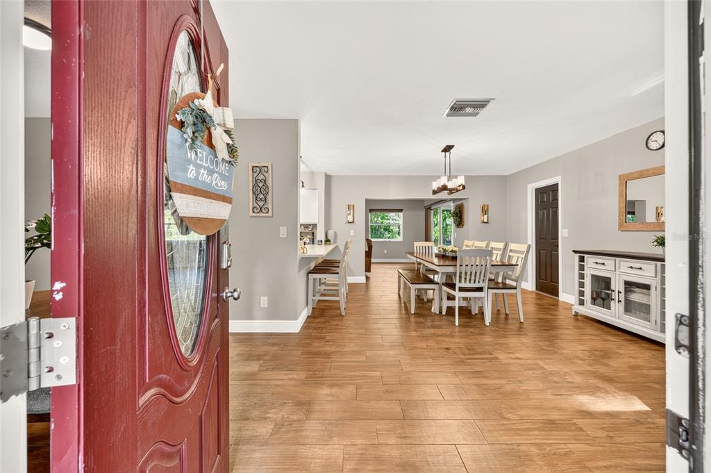 An open-concept dining area and kitchen feature wood-look tile flooring and a red front door — 1920 NW 15TH AVENUE, CRYSTAL RIVER, FL