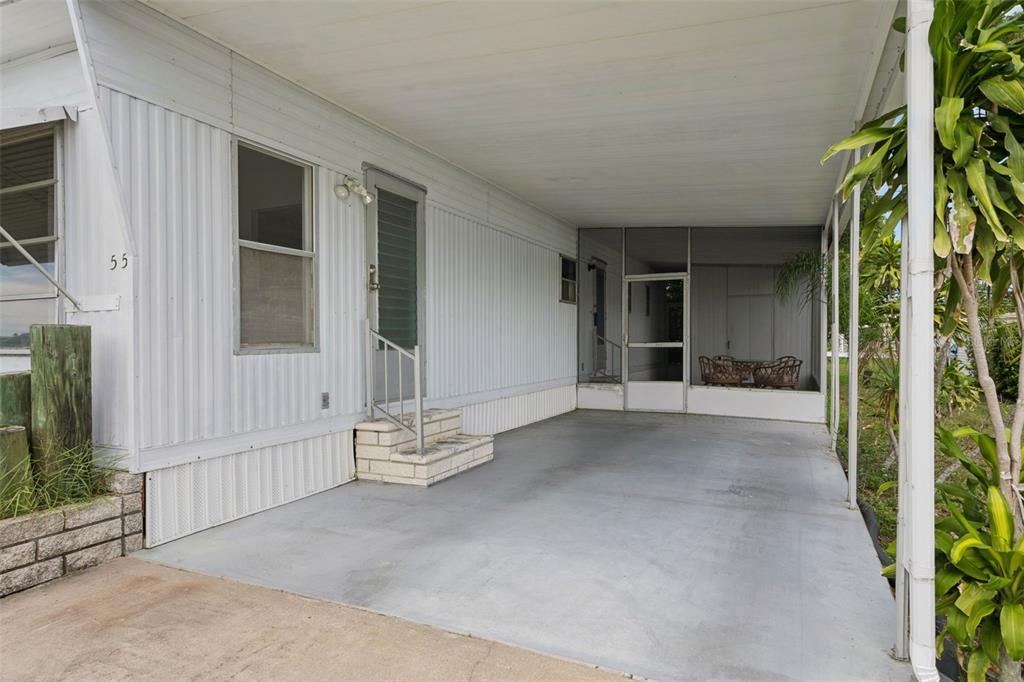 A mobile home exterior features a concrete carport, a screened-in porch, and white metal siding — 55 LEXINGTON COURT UNIT 12, PALM HARBOR, FL