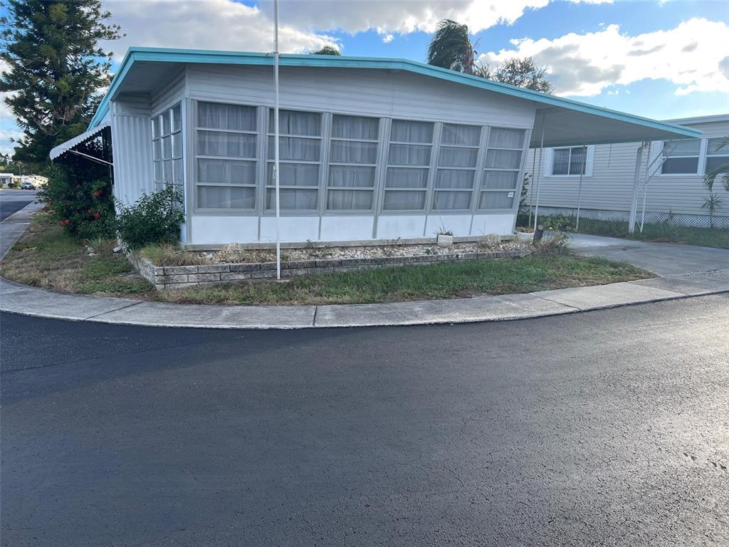 A single-story mobile home features a screened-in porch, a metal roof, and a carport — 201 ROYAL PALM CIRCLE, LARGO, FL