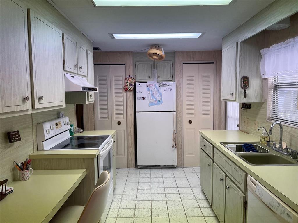 A galley-style kitchen features light wood-grain cabinets, laminate countertops, white appliances, and tiled flooring — 201 ROYAL PALM CIRCLE, LARGO, FL