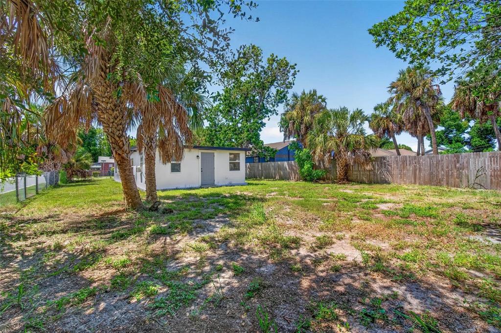 A small white house sits in a grassy backyard with palm trees and a wooden fence — 1901 MELROSE AVENUE S, ST PETERSBURG, FL