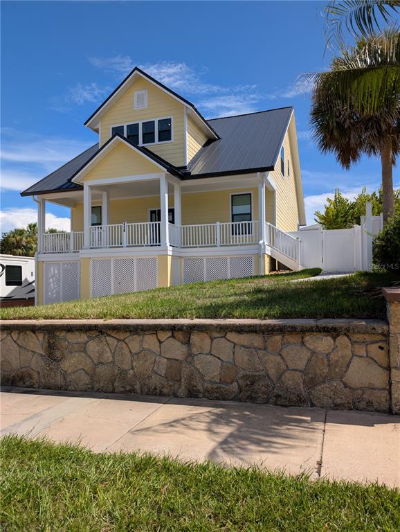 A yellow two-story house with a metal roof and a stone retaining wall in front — 414 JESSAMINE BOULEVARD, DAYTONA BEACH, FL
