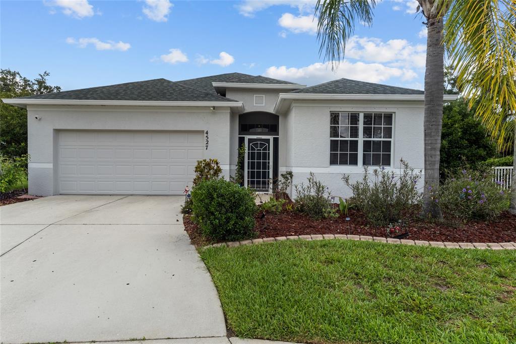 A single-story house with a white stucco exterior, a two-car garage, and a palm tree — 4527 FERRYS MILL PLACE, ELLENTON, FL