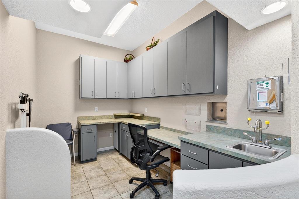 A medical exam room features gray cabinetry, a laminate countertop with a sink, and tile flooring — 1318 S EUSTIS STREET, EUSTIS, FL