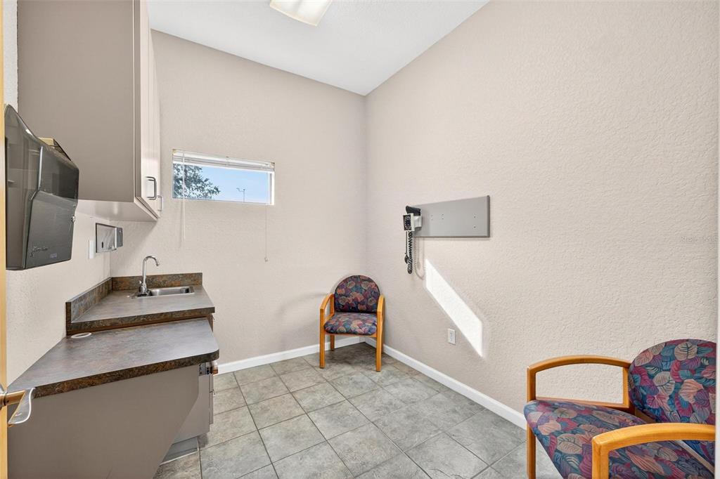 A small medical examination room features a sink, cabinetry, two patterned chairs, and tile flooring — 1318 S EUSTIS STREET, EUSTIS, FL