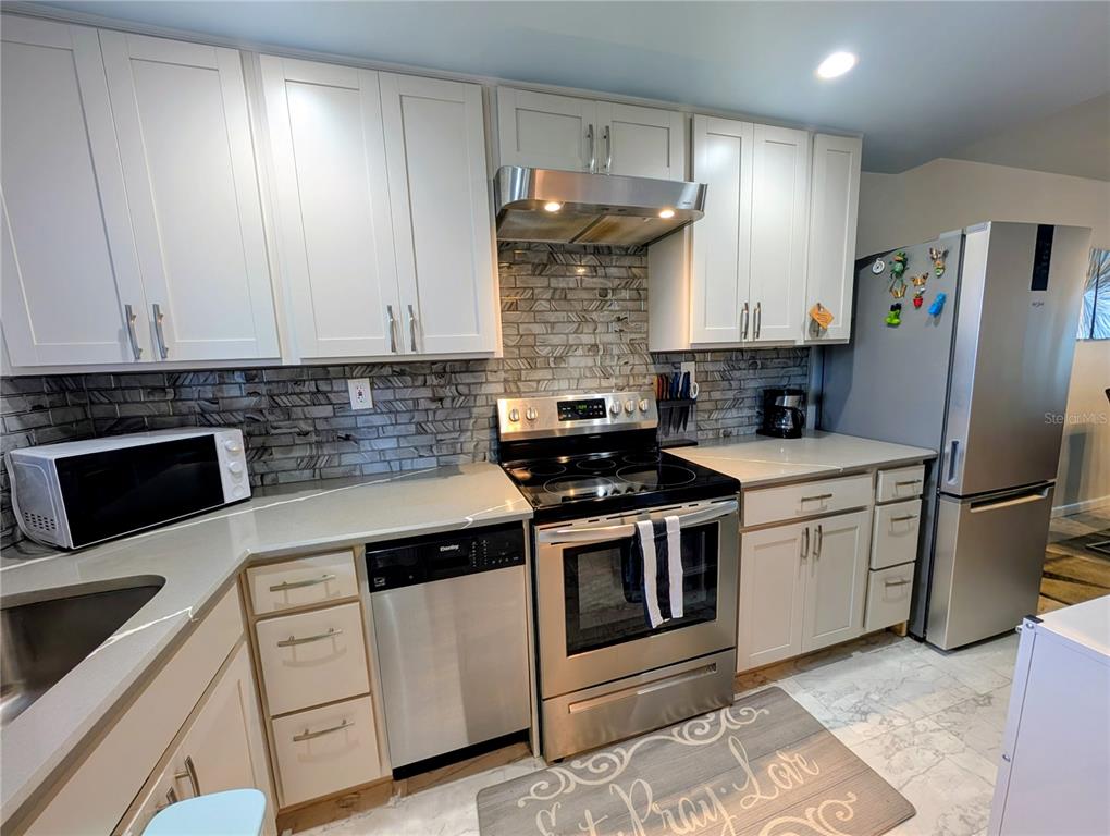 A dining area with a glass table and white chairs sits adjacent to a bar cart — 1243 S MARTIN LUTHER KING JR AVENUE UNIT B205, CLEARWATER, FL