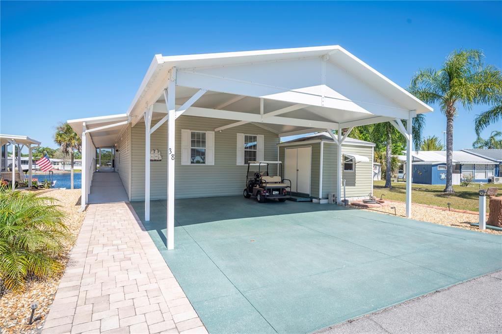 A single-story mobile home features a large carport, a paved walkway, and a storage shed — 38 QUEEN OF WATERS STREET, LAKE WALES, FL