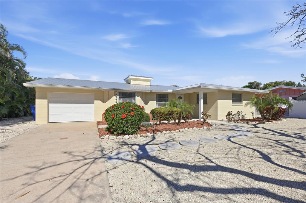 A single-story yellow house with a metal roof, a garage, and a gravel front yard — 109 TERN DRIVE, ANNA MARIA, FL