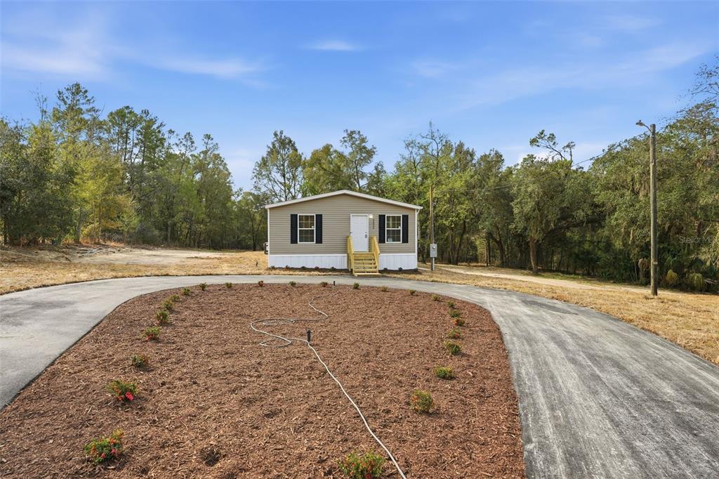 A single-story manufactured home sits behind a circular driveway with a landscaped center island — 25924 WHIPPERWILL STREET, BROOKSVILLE, FL