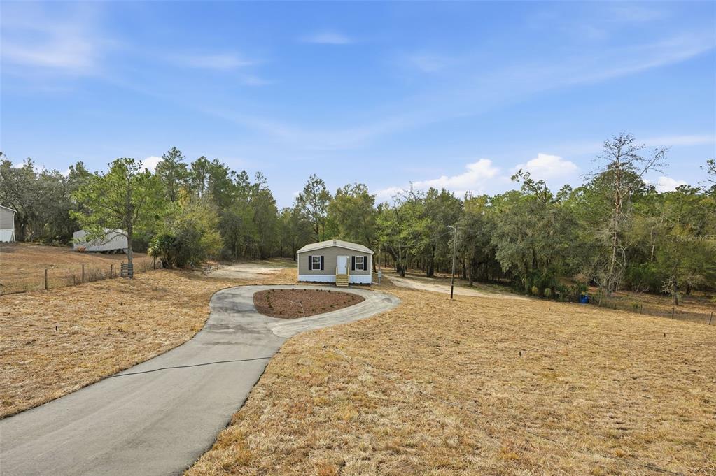 A small, light-colored house sits at the end of a circular driveway on a grassy lot — 25924 WHIPPERWILL STREET, BROOKSVILLE, FL