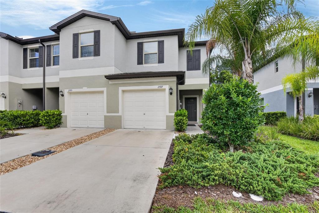 A two-story townhouse exterior features a two-car garage, gray siding, and a small front yard — 2597 CHARLAN, HOLIDAY, FL