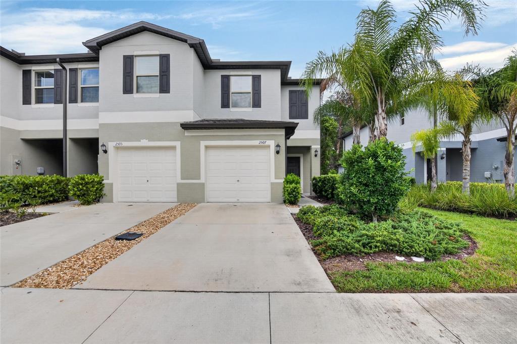 A two-story townhouse exterior with two garage doors, light gray siding, and palm trees — 2597 CHARLAN, HOLIDAY, FL