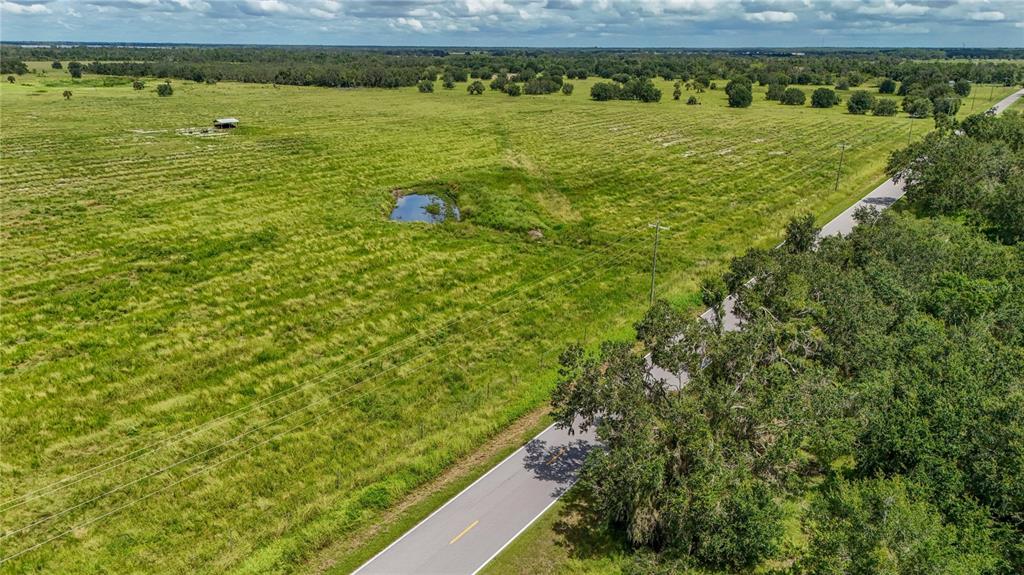 An aerial view shows a grassy field with a small pond and a paved road — GOUGH ROAD, ONA, FL