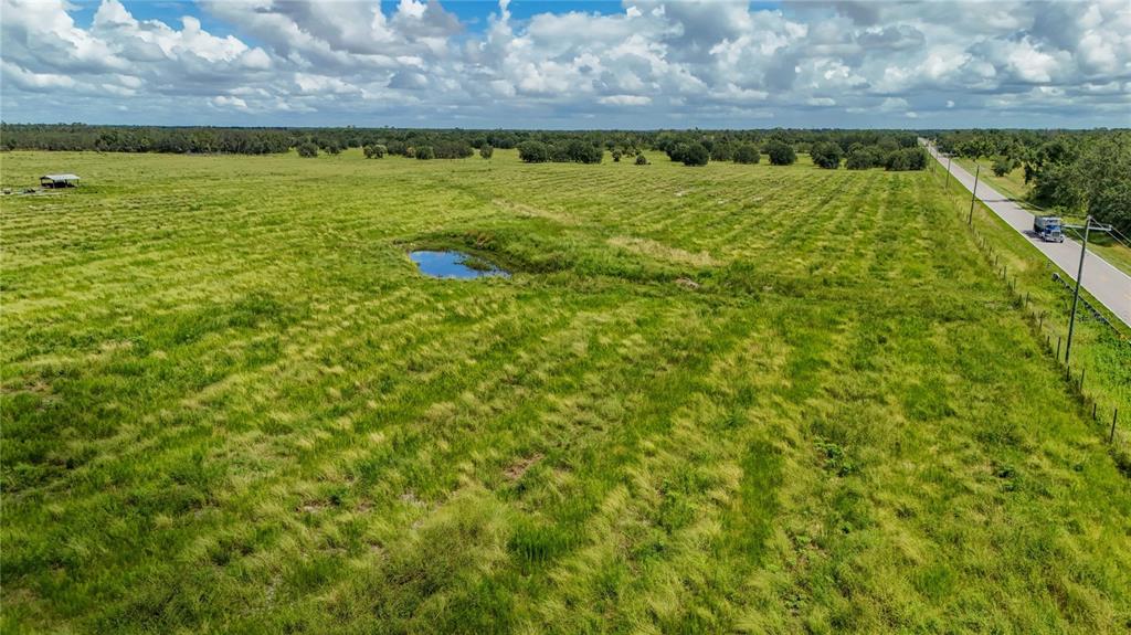 An aerial view shows a large, grassy field with a small pond and a road — GOUGH ROAD, ONA, FL